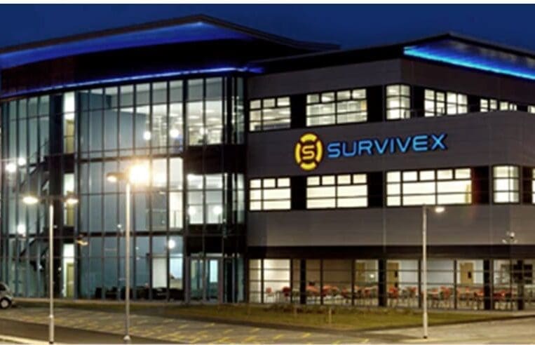 A modern office building at night, featuring large glass windows and a prominent "Survivex" logo illuminated in blue and yellow on the facade. The well-lit building is part of the 3t Energy Group, with the parking lot in front mostly empty, reflecting its commitment to advanced AIS and training services.