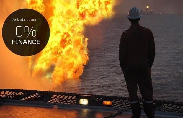 A person in protective gear is standing on a platform, facing a large fire at sea. A circular black graphic with the text "Ask about our 0% FINANCE for Training Courses" overlays the upper left part of the image.