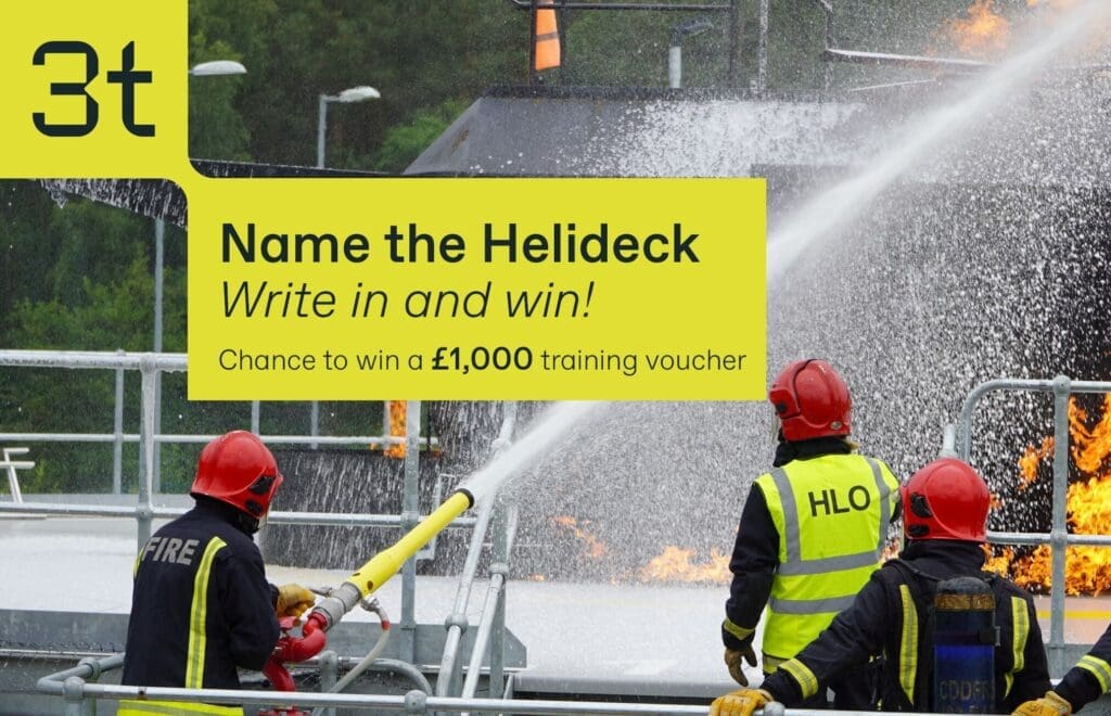 Three firefighters in protective gear are using hoses to spray water on a fire on a helideck. A banner reads "3t Name the Helideck. Write in and win! Chance to win a £1,000 firefighting training voucher." One firefighter wears a vest labeled "HLO.